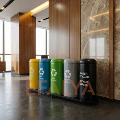 Lüks bir plaza lobisinde, mermer duvar ve ahşap paneller önünde, ortak bir kaide üzerinde sıralanmış; plastik, kağıt, cam, metal ve diğer atıklar için farklı renklerde 5’li silindirik sıfır atık kutusu seti.