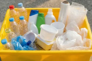 Sarı geri dönüşüm kutusu içerisine atılmış şeffaf PET su şişeleri, beyaz deterjan kutuları, plastik gıda kapları ve baloncuklu naylon ambalaj atıkları.